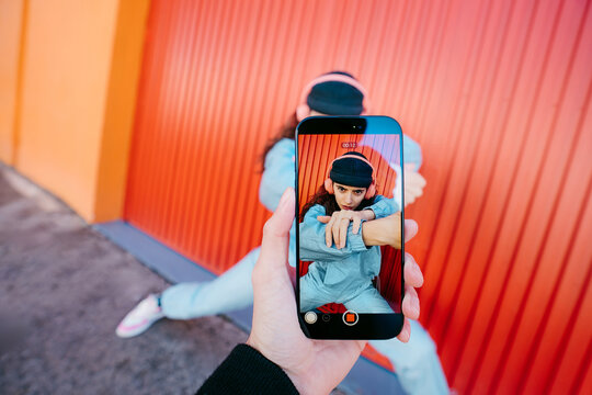 Woman Posing In Front Of Colorful Red Wall Seen Through Phone Screen
