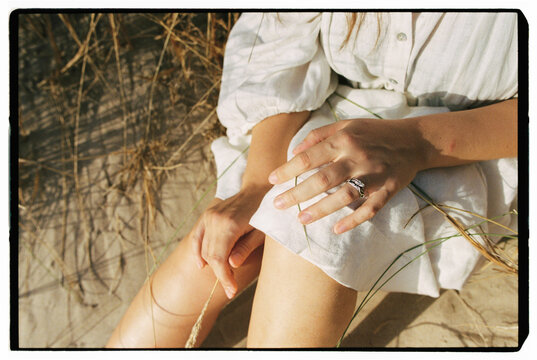 Woman hands resting on white dress in sand dunes