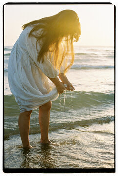 Woman wringing out wet dress in ocean at sunset