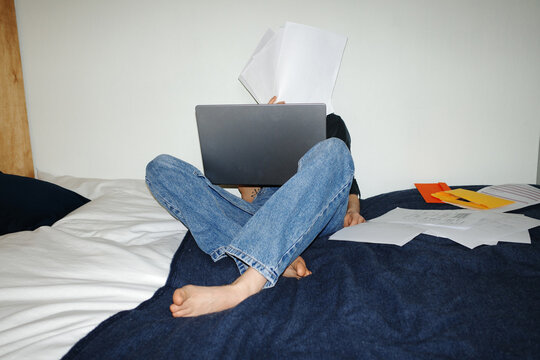 Person feeling stressed paying bills, covering face with documents