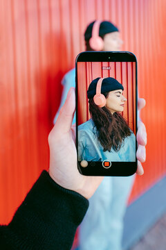 Woman Posing In Front Of Colorful Red Wall Seen Through Phone Screen