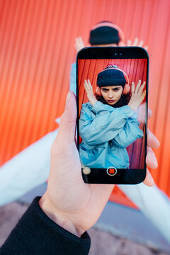 Woman Posing In Front Of Colorful Red Wall Seen Through Phone Screen