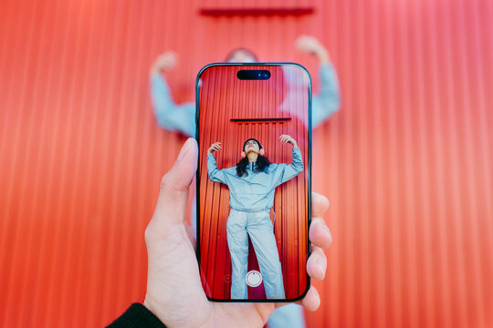 Woman Posing In Front Of Colorful Red Wall Seen Through Phone Screen