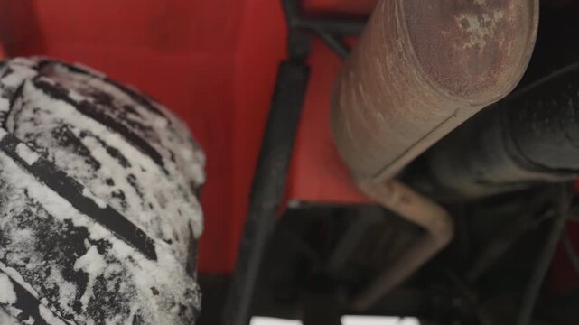 Closeup exhaust and tire underbody, rusty muffler emits visible steam in cold air while heavy tread packs snow, low angle shots show undercarriage and suspension motion, industrial mechanical detail