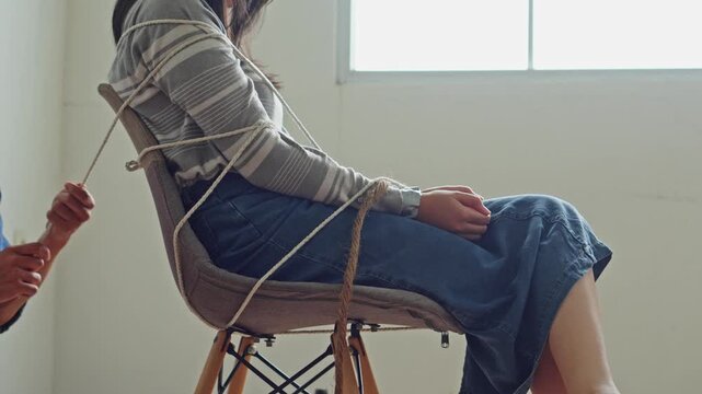 Cinematic side view of hostage victim bound to chair by unidentified captor in balaclava