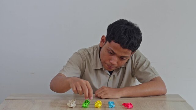 Asian man in shirt demonstrating repetitive behavior by organizing colored paper scraps on desk