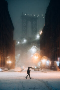 Pedestrian Walking in Snowstorm Near Brooklyn Bridge at Night
