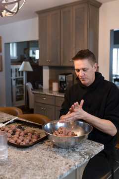 Man sitting in kitchen rolling meatballs.