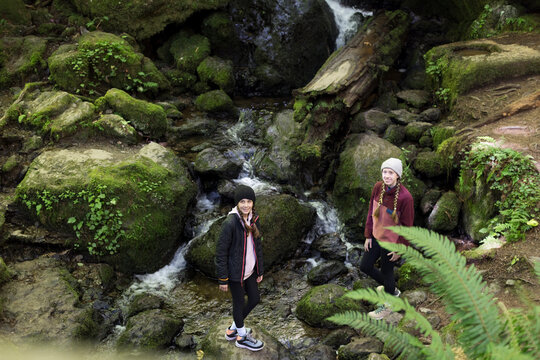 Two sisters by a small waterfall in the woods. 