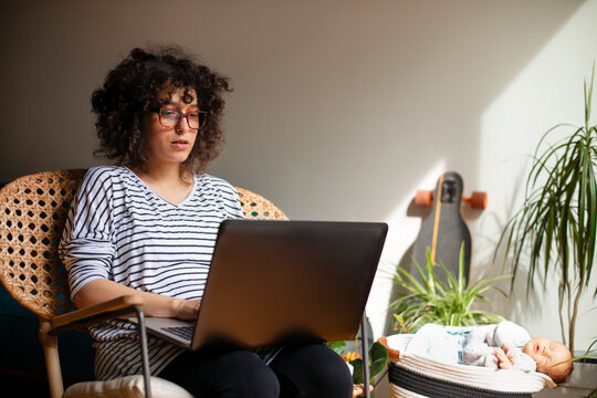 Working Mother With Laptop And Sleeping Newborn At Home