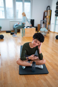 Woman checking smartphone during workout break in fitness studio