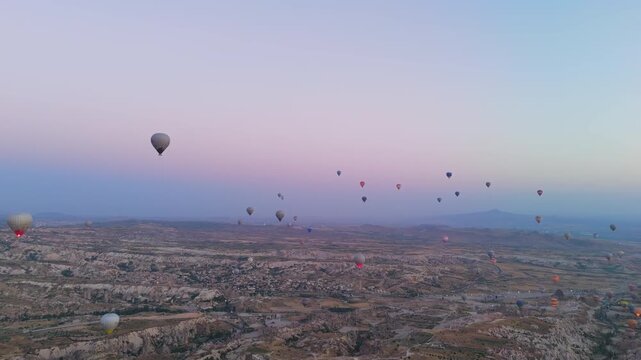 Goreme, Nevsehir, Turkey. Massive armada of hot air balloons with fire bursts flying at dawn over Goreme town and Cappadocia landscape in panoramic view. Aerial View