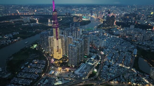High altitude drone shot highlighting clusters of high-rise buildings surrounded by dense urban blocks, highway intersections, and glowing riverside skyline at evening in Saigon.