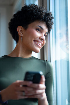 Woman smiling at window with phone