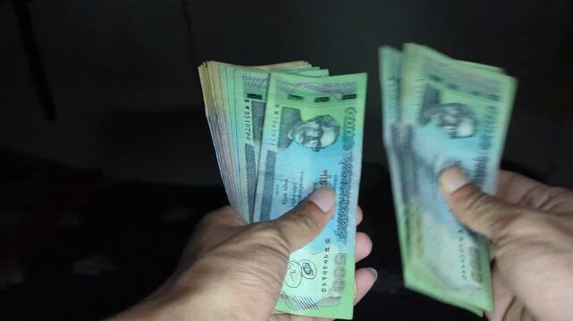 Person counting stack of bangladeshi taka five hundred and one thousand notes in dark lighting closeup view of hands holding currency bills showing financial transaction or savings concept.