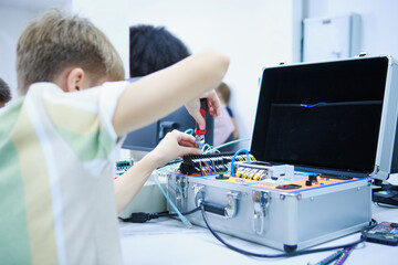 Young boy intently soldering a circuit board component with silver equipment and electronic tools...