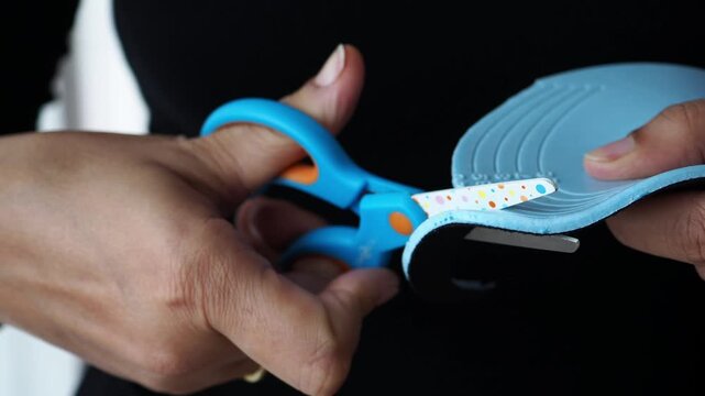 A person uses scissors to cut a piece of shoe sole.