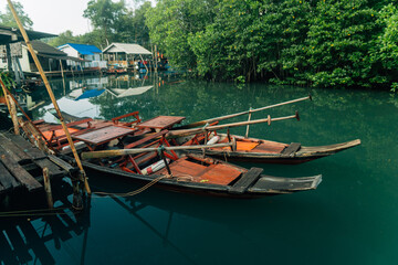 Obraz premium Traditional wooden boats and stilt houses along a calm canal surrounded by lush green mangrove forest.