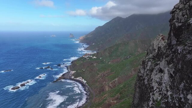 View from Roque de Las Animas cliff near the village of Taganana towards the ocean coast and the mountainous terrain of Anaga Rural Park. Canary Islands. Tenerife. Aerial video. 4K 50fps.