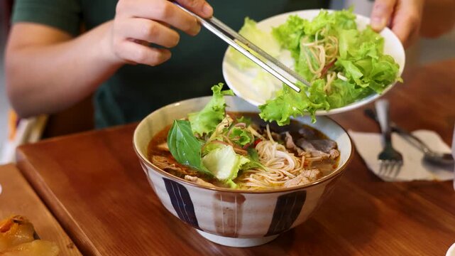 Asian Person Adding Fresh Lettuce to Bun Cha Noodle Soup with Chopsticks