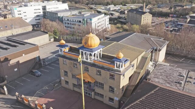 Sikh temple Gurdwara Guru Nanak Gurdwara in Huddersfield Kirklees West Yorkshire England United Kingdom with golden domes and Nishan Sahib flag, drone ascent shot