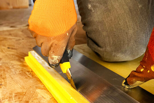 Worker cutting blue polystyrene foam heat insulation with old retractable utility knife, closeup detail