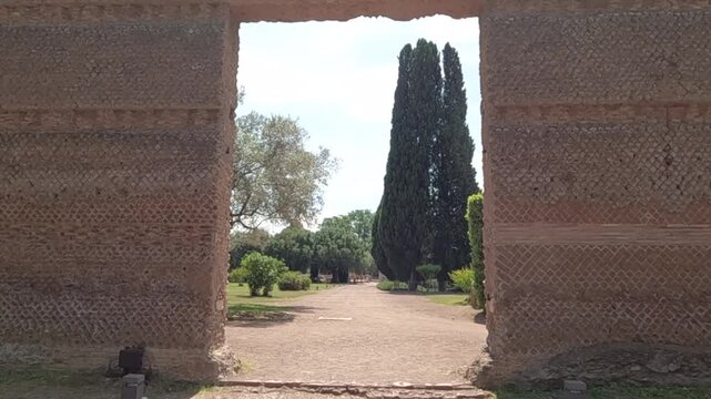Monumental ancient Roman brick doorway frames a scenic garden path with tall cypress trees at Villa Adriana, Hadrian's Villa near Tivoli, Rome, Italy.