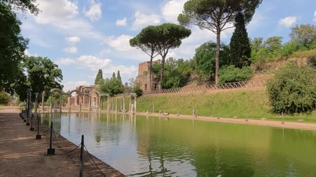 Serene reflecting pool at Villa Adriana, Hadrian's Villa in Tivoli near Rome. Ancient Roman columns and ruins line the tranquil green water surrounded by Mediterranean pine trees.