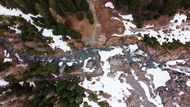 Aerial: river near Engstligen Falls with snow during the day, second highest waterfall in Switzerland, top down drone shot