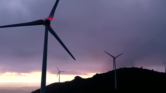 Wind farm Serra da Boneca with Nordex turbines glowing red at twilight, generating clean renewable energy beneath a dramatic, colorful dusk sky for a sustainable future, close up push in drone shot