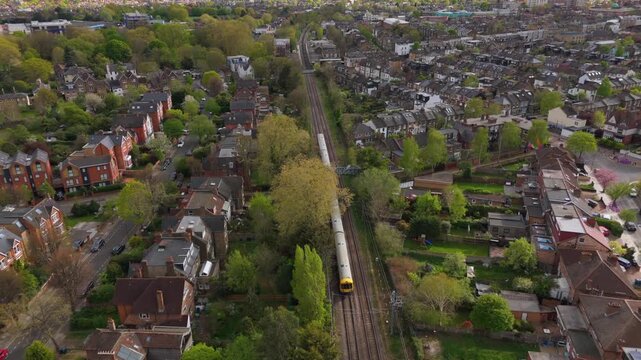 Drone following train travelling through suburban British town. London Overground Mildmay Line