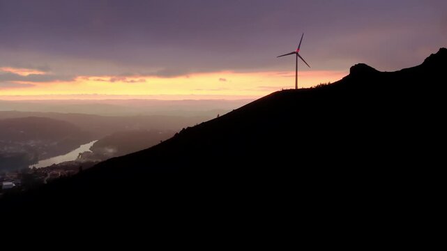 Wind turbine horizontal axis type on Serra da Boneca ridge in Centro region Portugal overlooking Mondego River valley at sunset representing renewable energy transition, static silhouette shot