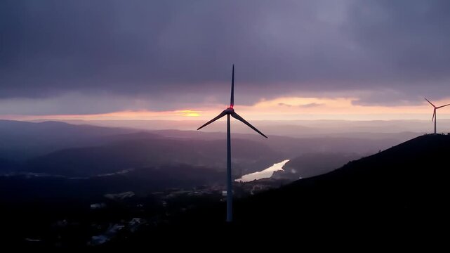 Wind turbine horizontal axis type rotating on Serra da Boneca ridge in Centro region Portugal over Mondego River valley under stratiform cloud sky indicating steady wind conditions, drone push in shot