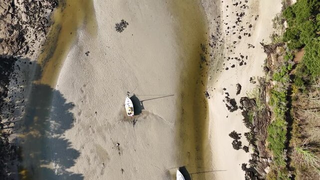 Drone descends over sailboats stranded on sandy tidal flats at low tide near Concarneau, Brittany, France. Bright sunny day, calm serene atmosphere.