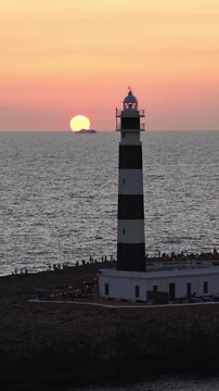Vertical Drone Flyby Lighthouse with Tourists at Sunset, Water Reflections Punta Nati Menorca