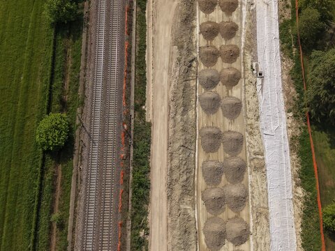 Railway Construction Site: An aerial view of a railway under construction, featuring parallel tracks, piles of gravel, and cleared land, highlighting the infrastructure development process.