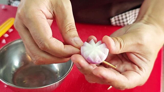 Close up of chef's hands delicately carving a red shallot into a beautiful flower shape.&nbsp;