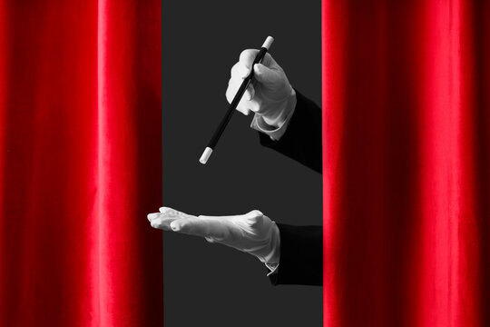 Magician's hands with wand behind red curtains on dark background