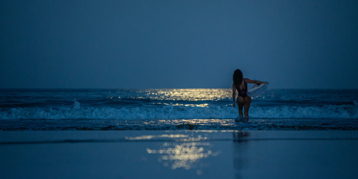 Surfer female surfing at night with full moon illuminating the ocean