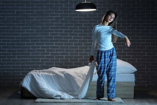 Female sleepwalker with blanket near bed against black brick wall in dark bedroom at night
