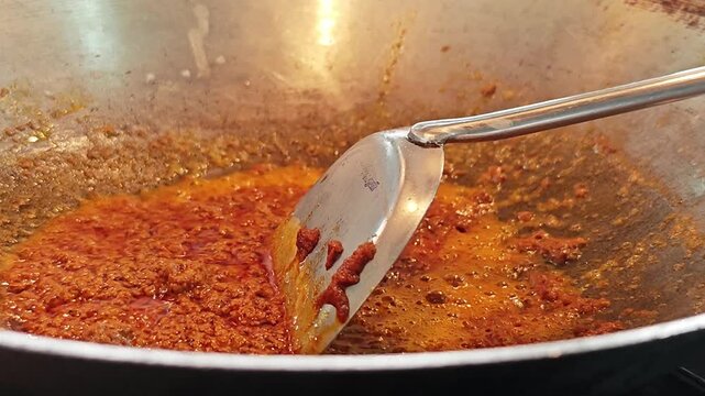 Saut&eacute;ing Thai red curry paste in hot oil, an essential step for authentic Thai curry preparation.