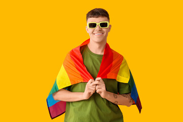 Fototapeta premium Handsome young happy man with LGBT flag on yellow background