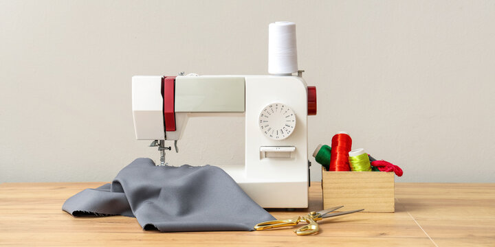Modern sewing machine with tailor's supplies on wooden table