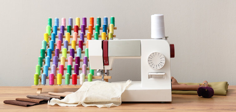 Modern sewing machine with different colorful threads and supplies on wooden table