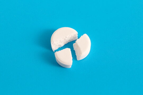 On a blue background lies a white medicinal tablet, broken into three parts.