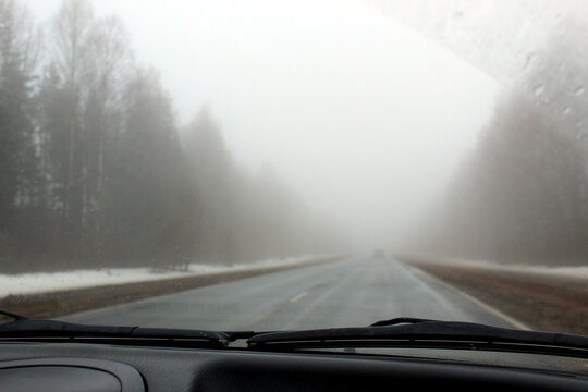 From the car's interior, the highway covered in fog is visible.