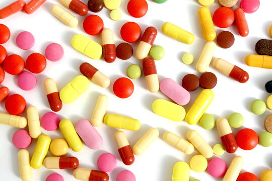 Texture of multi-colored medicine tablets and capsules lie on a white background.