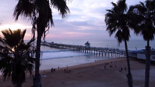 Pier Overlooking the Sunset on beach. San Clemente, Orange County, California. Cinematic Silhouette of Palm Trees in the foreground