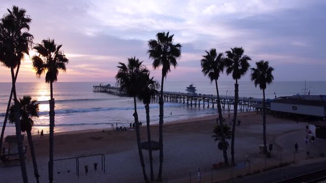 Pier Overlooking the Sunset on beach. San Clemente, Orange County, California. Cinematic Silhouette of Palm Trees in the foreground.