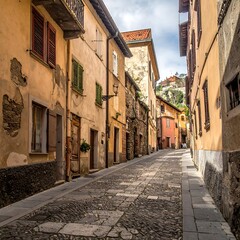 Obraz premium Cobblestone street winds past weathered buildings in a sunny European town